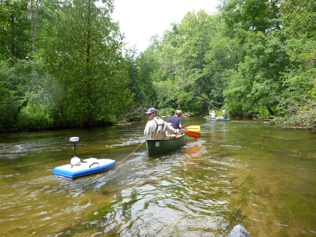 MSU Hydrogeology group collecting data in a canoe on a river surrounded by trees